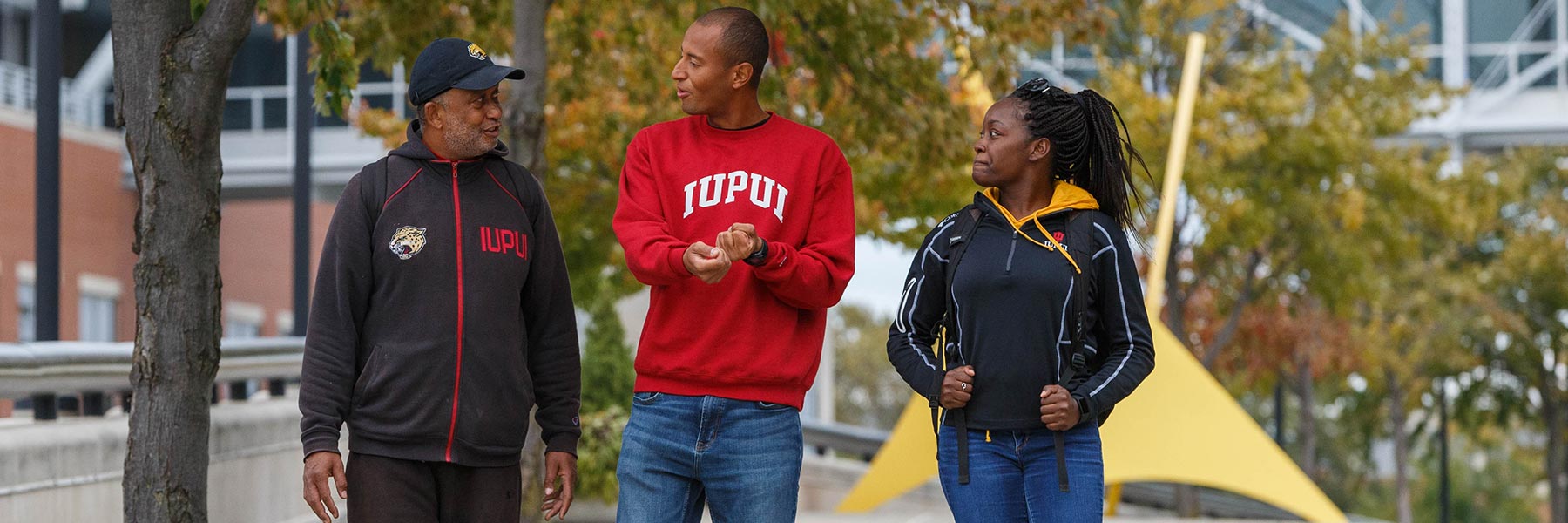 Three people have a conversation as they walk on campus.